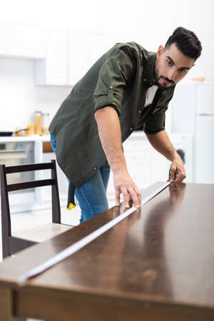 Arabian carpenter measuring blurred wooden table in kitchenの写真素材