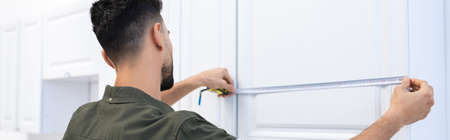 Arabian man with tape measure measuring kitchen cabinet, bannerの写真素材