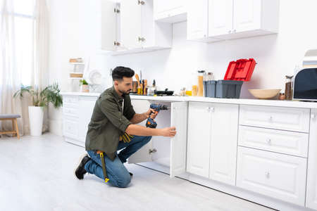 Young arabian man with screwdriver fixing door of kitchen cabinetの写真素材