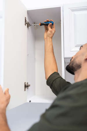 Blurred muslim man with screwdriver fixing hinge in cabinet in kitchen at homeの写真素材