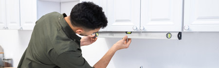 Arabian man measuring kitchen cupboard with spirit level at home, bannerの写真素材
