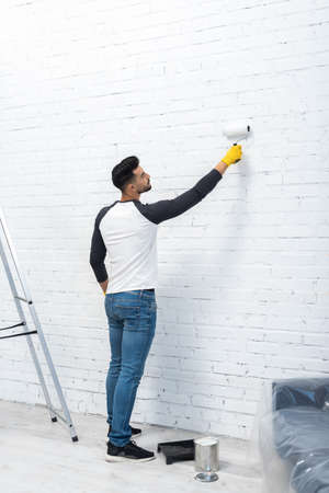 Side view of young muslim man coloring wall near dye and ladder at homeの写真素材