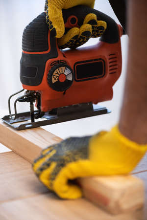 Cropped view of man in gloves sawing board at homeの写真素材