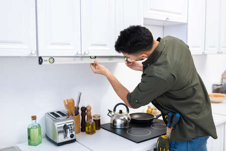 Muslim man checking kitchen cupboard with spirit level near worktopの写真素材