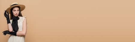 Stylish young woman in sun hat and gloves posing and looking away isolated on beige, bannerの写真素材