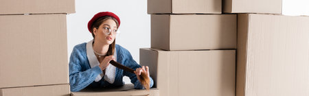 Pretty woman in cardigan and beret touching hair between cardboard boxes isolated on white, bannerの写真素材