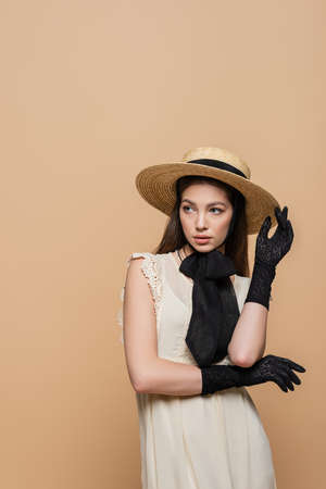 Pretty woman in straw hat and black gloves posing isolated on beigeの写真素材