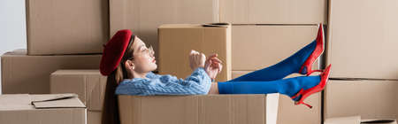 Side view of stylish woman sitting in cardboard box on white background, bannerの写真素材