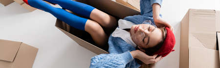Top view of woman in eyeglasses holding beret while sitting in package on white, bannerの写真素材
