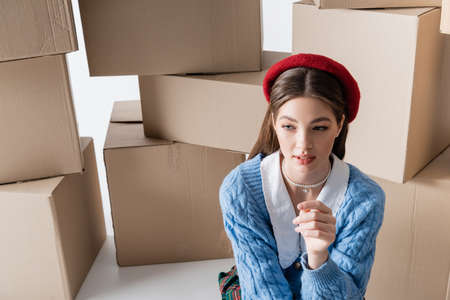Pretty model in beret looking away near cardboard boxes on white backgroundの写真素材
