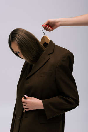 woman holding hanger with model in brown blazer isolated on grey