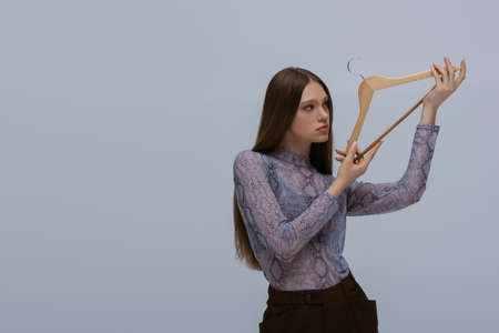 brunette teenage model holding wooden hanger isolated on greyの写真素材