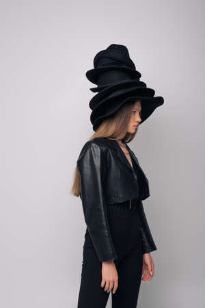 side view of brunette model in leather jacket and different black hats on head isolated on greyの写真素材