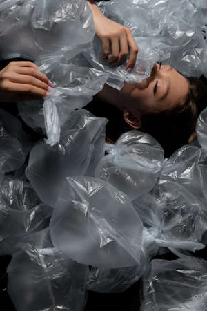 top view of model with closed eyes lying around plastic bags, recycle fashion concept