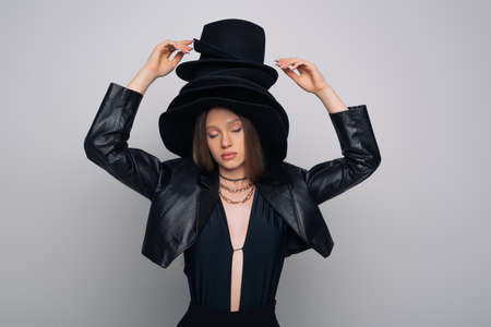 brunette model with closed eyes touching black hat on head isolated on greyの写真素材
