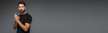 portrait of confident and bearded man in black t-shirt looking away isolated on grey, bannerの写真素材