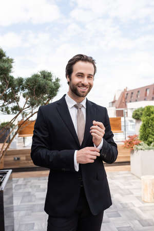 Smiling groom adjusting shirt on terrace outdoors
