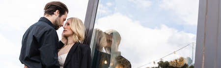 Low angle view of brunette man kissing girlfriend in jacket on terrace, bannerの写真素材