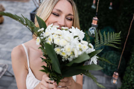 Blonde bride covering face with blurred bouquet on terraceの写真素材