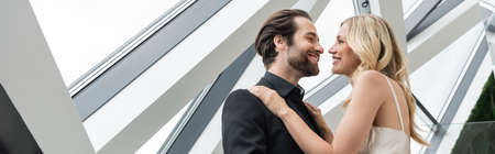 Low angle view of elegant couple smiling at each other while hugging in restaurant, banner