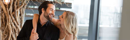 Cheerful woman hugging and looking at boyfriend in restaurant, banner
