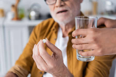 Cropped view of african american nurse holding glass of water near blurred pensioner with pill at homeの写真素材