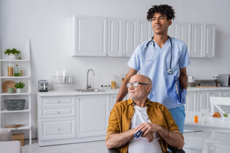 Positive african american nurse holding clipboard near pensioner with pulse oximeter at homeの写真素材
