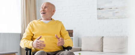 Happy senior man sitting in wheelchair in living room, bannerの写真素材