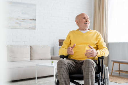 Positive elderly man looking away while sitting in wheelchair at home
