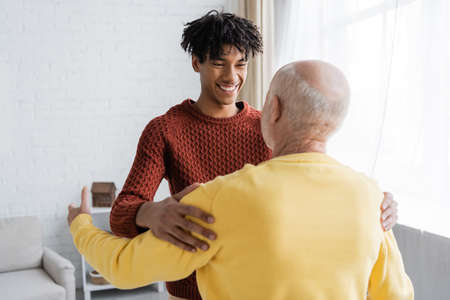 Smiling african american man hugging and looking at blurred granddad at home