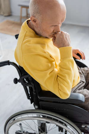 Sad pensioner sitting in wheelchair in living roomの写真素材