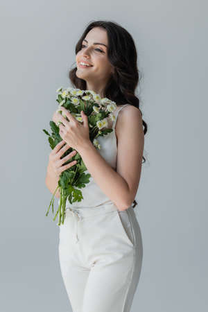 Cheerful woman holding bouquet and looking away isolated on greyの写真素材