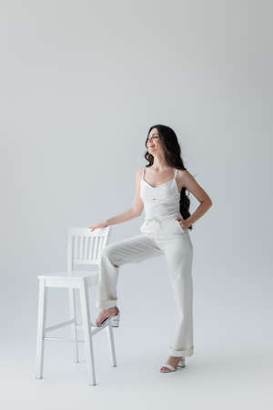 Smiling woman in white clothes posing near chair on grey backgroundの写真素材