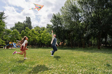 Asian father holding flying kite while running with daughter in parkの写真素材