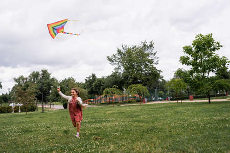 Happy asian girl holding flying kite while running in parkの写真素材