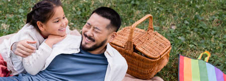Positive asian kid looking at dad near flying kite and wicker basket in park, bannerの写真素材