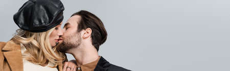 blonde woman in stylish beret kissing bearded man isolated on grey, bannerの写真素材