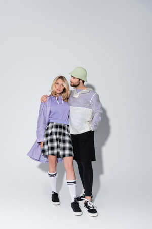 full length of bearded man in panama hat hugging stylish woman in tartan skirt and longs socks with sneakers on greyの写真素材