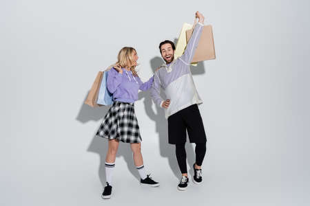 full length of excited man and cheerful woman in tartan skirt holding shopping bags on greyの写真素材