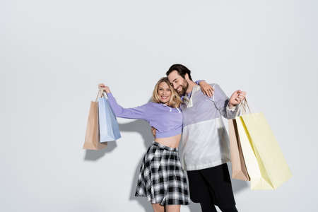 happy man and blonde woman in tartan skirt holding shopping bags on greyの写真素材
