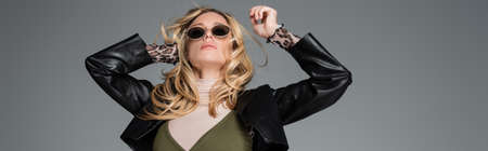 blonde model in black leather jacket and stylish sunglasses posing isolated on grey, banner
