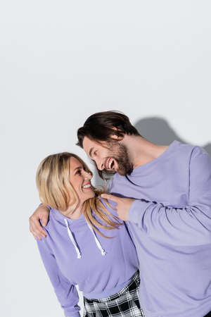 happy bearded man in purple sweatshirts pointing at blonde woman on grey