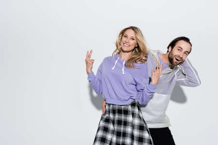 excited man near cheerful woman in purple sweatshirt showing peace sign on greyの写真素材