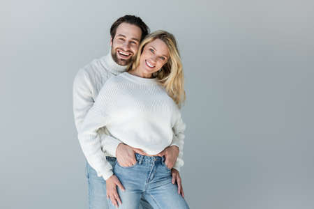 happy couple in white sweaters and denim jeans posing isolated on greyの写真素材