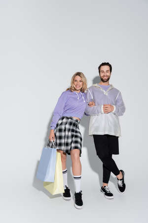 full length of happy and stylish couple holding shopping bags on grey