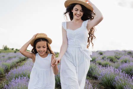 smiling girl and woman in white dresses and straw hats holding hands in fieldの写真素材