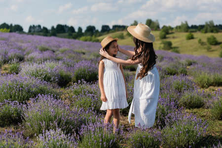 woman with long hair adjusting straw hat on daughter in fieldの写真素材