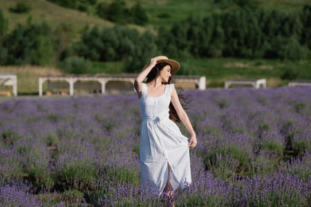 woman in white dress and straw hat posing in field with blossoming lavenderの写真素材