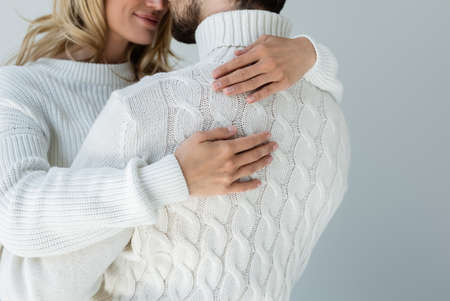 cropped view of cheerful woman in white sweater hugging with boyfriend isolated on greyの写真素材