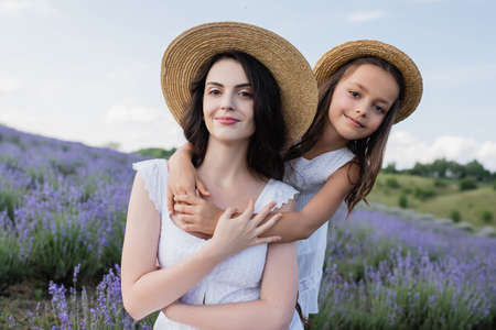 happy girl in straw hat hugging mother in blurred fieldの写真素材